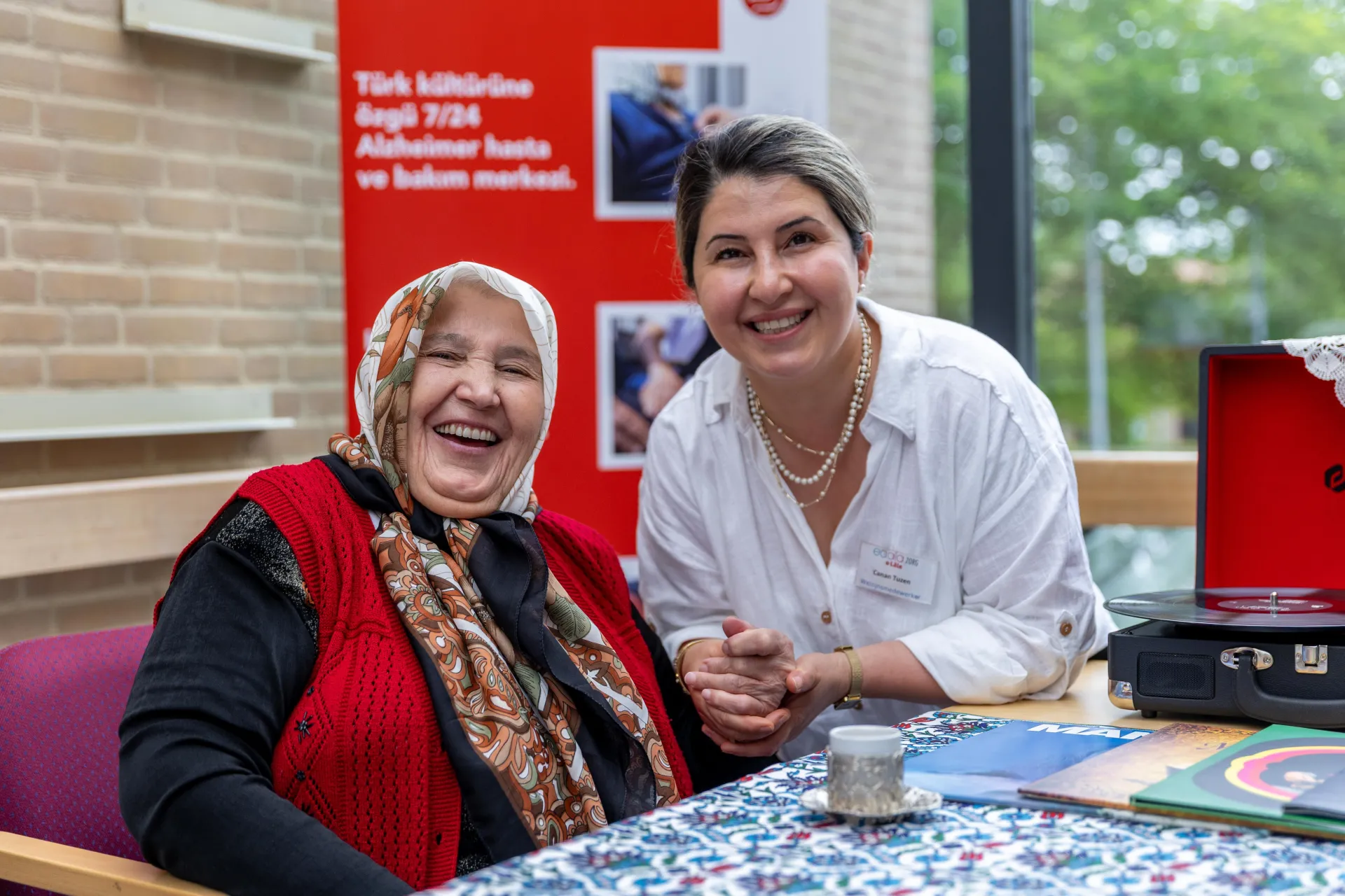Twee vrouwen glimlachen samen aan een tafel.